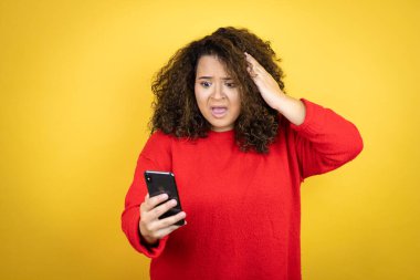 Sarı arka plan üzerine kırmızı kazak giyen genç Afro-Amerikalı kadın telefonda endişeli bir ifadeyle sohbet ediyor.