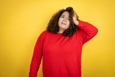 Sarı arka plan üzerine kırmızı kazak giyen Afro-Amerikalı genç bir kadın bir elini kafasına koyup sanki bir şey unutmuş gibi gülümsüyordu.