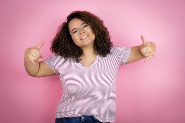 Pembe arka planda kırmızı çizgili tişört giyen genç Afrikalı Amerikalı kadın çılgın bir ifadeyle elleri havada rock sembolü yapıyor.