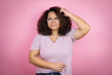 Pembe arka planda kırmızı çizgili tişört giyen Afro-Amerikalı genç bir kadın soru işaretlerini merak ediyor. Şüpheyle karışık, kafa kafaya düşünerek.