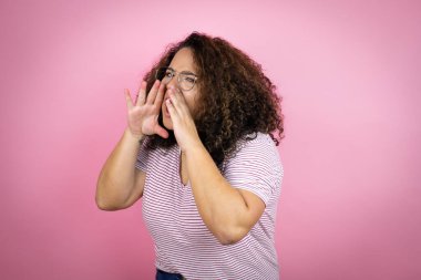 Genç Afrikalı Amerikalı kadın pembe arka planda kırmızı çizgili tişört giyip elleri ağızda bağırıyor ve bağırıyordu.