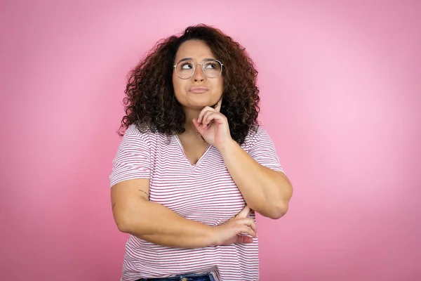 Pembe arka planda kırmızı çizgili tişört giyen Afro-Amerikalı genç bir kadın. Ciddi bir yüz ifadesi var. Elleri çenesinde soru sormayı düşünüyor.