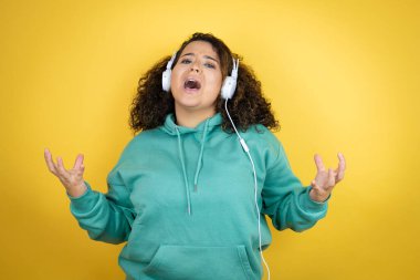 Genç Afrikalı Amerikalı kız spor kıyafetleri giyip kulaklık takıyor. Deli gibi bağırıyor ve bağırıyor. Saldırgan ifadeler ve kollar havada. Hayal kırıklığı konsepti.