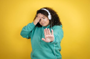 Genç Afrikalı Amerikalı kız spor kıyafetleri giyiyor, kulaklık takıyor ve üzgün ve korku ifadeleriyle jest yapıyor. Utanç verici ve olumsuz bir kavram.