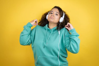 Spor kıyafetleri giyen ve kulaklık takan Afro-Amerikan genç kız tişörtünü başarılı bir ifadeyle tutuyor.