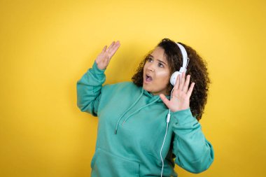 Genç Afrikalı Amerikalı kız spor kıyafetleri giyiyor ve kulaklık takıyor. Kolları havada, sanki yukarıdan bir şey düşmüş gibi.