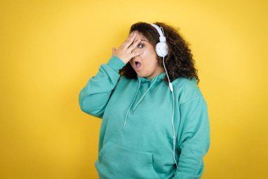 Afrika kökenli Amerikalı genç bir kız spor kıyafetleri giyiyor ve kulaklık takıyor. Şok olmuş bir şekilde yüzünü ve gözlerini kapatıyor. Utanmış bir ifadeyle parmaklarından bakıyor.