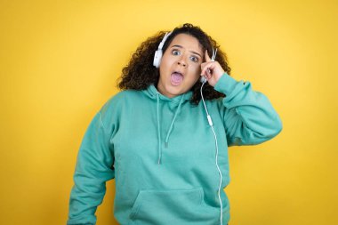 Spor kıyafetleri giyen, kulaklık takan, gülümseyen ve kafasında parmaklarıyla bir fikri olduğunu düşünen Afro-Amerikalı genç bir kız..