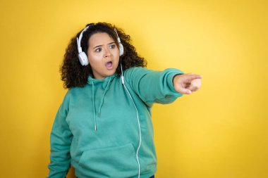 Genç Afrikalı Amerikalı kız spor kıyafetleri giyiyor ve kulaklık takıyor. Parmağıyla işaret ediyor. Şaşırmış, ağzı açık.