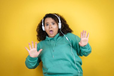 Afrika kökenli Amerikalı genç bir kız spor kıyafetleri giyiyor ve kulaklık takıyor. Korkudan dehşete düşmüş ve korkmuş bir şekilde. El hareketlerini durdur, şok içinde bağır. panik konsepti.