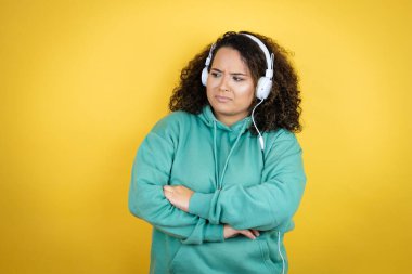 Genç Afrikalı Amerikalı kız spor kıyafetleri giyiyor ve kulaklık takıyor. Kollarını kavuşturmaktan sıkılmış ve yorgun görünüyor.