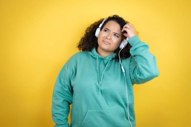 Genç Afrikalı Amerikalı kız spor kıyafetleri giyiyor ve kulaklık takıyor. Soruları karıştırıyor ve merak ediyor. Şüpheyle karışık, kafa kafaya düşünerek.