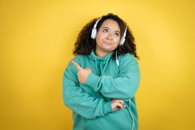 Genç Afrikalı Amerikalı kız spor kıyafetleri giyiyor ve kulaklık takıyor. Kafası karışmış ve eli ve parmağı kenarı işaret ediyor.