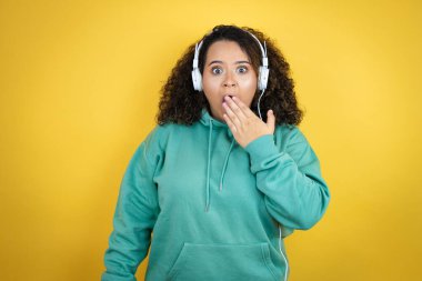 Genç Afro-Amerikalı kız spor kıyafetleri giyiyor ve kulaklık takıyor. Ağzı elle kapatıyor, şok geçiriyor ve hata yapmaktan korkuyor. şaşırmış ifade