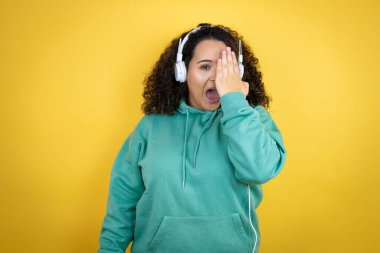 Genç Afrikalı Amerikalı kız spor kıyafetleri giyiyor ve kulaklık takıyor. Bir gözünü eliyle kapatıyor. Yüzünde kendine güvenen bir gülümseme ve şaşırtıcı bir duygu var..