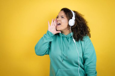 Genç Afrikalı Amerikalı kız spor kıyafetleri giyiyor ve kulaklık takıyor. Bağırıyor ve ağızdan ağıza bağırıyor.