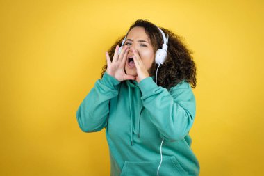 Genç Afrikalı Amerikalı kız spor kıyafetleri giyip kulaklık takıyor ve elleri ağızda bağırıyor.
