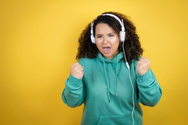 Genç Afrikalı Amerikalı kız spor kıyafetleri giyiyor ve kulaklık takıyor. Çok mutlu ve heyecanlı. Kollarını kaldırıp, gülümseyerek ve başarı için bağırarak kazanan jestler yapıyor..