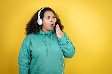 Genç Afro-Amerikalı kız spor kıyafetleri giyiyor ve kulaklık takıyor. Ağzı elle kapatıyor, şok geçiriyor ve hata yapmaktan korkuyor. şaşırmış ifade