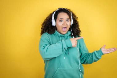 Genç Afrikalı Amerikalı kız spor kıyafetleri giyiyor ve kulaklık takıyor. Şaşırdı ve elindeki bir şeyi gösterip işaret ediyor.