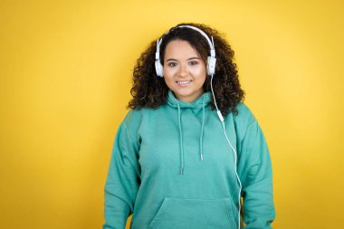 Genç Afrikalı Amerikalı kız spor kıyafetleri giyiyor ve kulaklık takıyor. Mutlu yüzlü, mutlu yüzlü, kendine güvenen bir gülümsemeyle dişlerini gösteriyor.