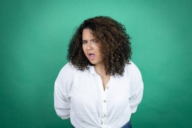 Genç Afro-Amerikalı kız yeşil arka planda beyaz gömlek giyiyor. Şaşırmış ve şaşırmış bir ifade, korku ve heyecanlı bir yüz ifadesi var..