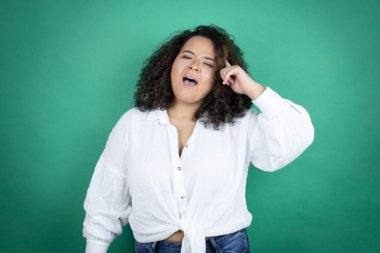 Genç Afro-Amerikalı kız yeşil arka planda beyaz gömlek giyiyor. Gülümsüyor ve parmakları kafasında bir fikri olduğunu düşünüyor..