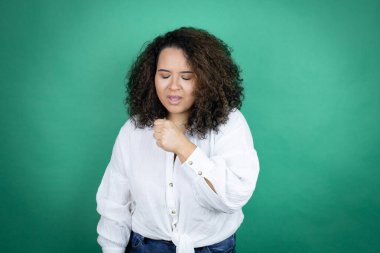 Genç Afro-Amerikalı kız, yeşil arka planda beyaz gömlek giyiyor ve eli ağzında, çünkü öksürüyor.