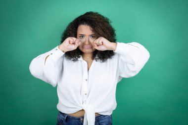 Genç Afro-Amerikalı kız, yeşil arka planda beyaz gömlek giyiyor. Depresyonda ve sıkıntıdan endişe ediyor. Kızgın ve korkmuş. Üzücü ifade.