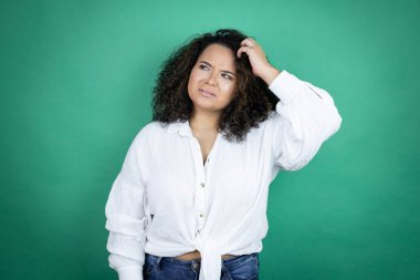 Genç Afro-Amerikalı kız yeşil arka planda beyaz gömlek giyiyor ve soru sormayı merak ediyor. Şüpheyle karışık, kafa kafaya düşünerek.