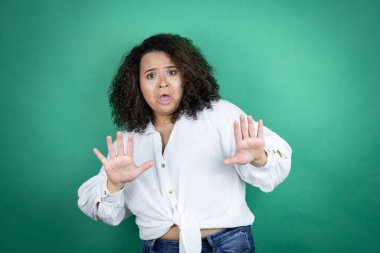 Yeşil arka planda beyaz gömlek giyen, korku ifadesinden korkan, dehşete düşmüş genç Afro-Amerikalı kız. El hareketlerini durdur, şok içinde bağır. Panik konsepti.