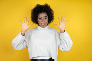 Sarı arka plan üzerine günlük süveter giyen Afro-Amerikalı kadın on numarayı gösterip gülümserken kendinden emin ve mutlu bir şekilde işaret ediyor.