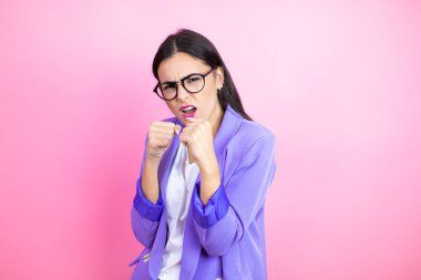 Pembe arka planda mor ceket giyen genç bir iş kadını. Yumruk yumruğa dövüşme, agresif ve öfkeli saldırı, tehdit ve şiddet.
