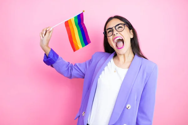 Pembe arka planda mor ceketli genç bir iş kadını homoseksüel gururu taşıyan çılgın bayrağı kutluyor ve kollarını kaldırmış ve gözleri açık bir şekilde haykırıyor. Kazanan kavram.