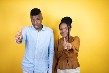 Sarı arka planda dikilen genç Afro-Amerikan çifti bir numaralı parmaklarıyla işaret ederken çok ciddiler.