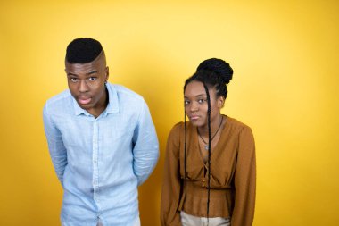 Genç Afro-Amerikan çifti sarı arka planda duruyor şaşkınlık ve şaşkınlık içinde bir ifade, korku ve heyecan dolu bir yüz..