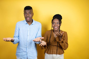 Genç Afro-Amerikan çifti sarı arka planda çılgın ve kızgın bir şekilde duruyor ve agresif bir ifadeyle bağırıyor ve kollarını kaldırıyor. Hayal kırıklığı konsepti.