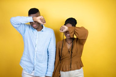 Genç Afro-Amerikan çifti sarı arka planda dikiliyor. Gözleri, kollarıyla gülüyor, neşeli ve komik. Kör kavram.