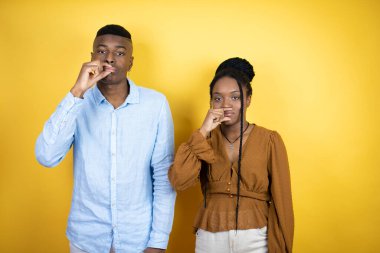 Genç Afro-Amerikalı çift sarı arka planın başında duruyor. Ağızları ve dudakları parmakları fermuar gibi kapalı. Gizli ve sessiz, tabu konuşması