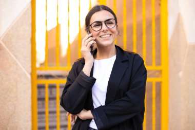Genç esmer kadın gülümsüyor. Şehirdeki akıllı telefondan konuşuyor..