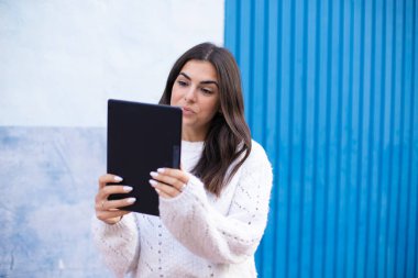 Genç esmer kadın şehirde tablet kullanarak mutlu bir şekilde gülümsüyor..