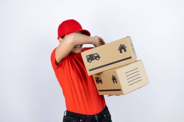 Kurye üniforması giyen genç ve güzel bir kadın teslimat paketleri taşıyor. Gözleri kollarıyla kapatıyor. Neşeli ve komik gülümsüyor. Kör kavram.