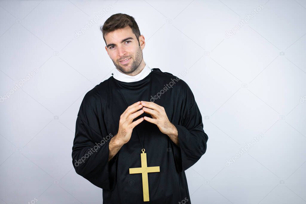 Young hispanic man wearing priest uniform standing over white background with Hands together and fingers crossed smiling relaxed and cheerful. Success and optimistic