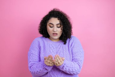 İzole edilmiş pembe arka planda sıradan bir süveter giyen genç ve güzel bir kadın avuçlarını birbirine değdirip gülümsüyor ya da el hareketi yapıyor. Tutun ve koruyun