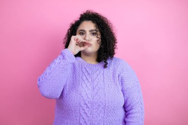 İzole edilmiş pembe arka plan ağzı ve dudakları parmaklarıyla fermuar gibi kapalı olan sıradan bir süveter giyen genç ve güzel bir kadın. Gizli ve sessiz, tabu konuşması