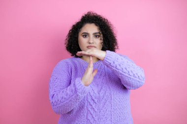 İzole edilmiş pembe arka plan üzerine günlük süveter giyen genç ve güzel bir kadın. Elleriyle, hayal kırıklığına uğramış ve ciddi bir yüz ifadesiyle jest yapıyor.