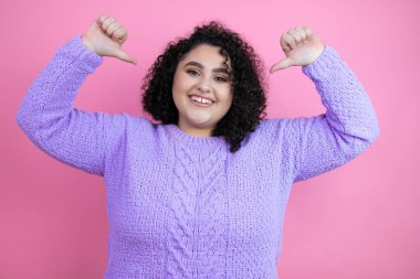 İzole edilmiş pembe arka planda sıradan bir süveter giyen genç ve güzel bir kadın. Kendine güvenen, gülümseyen, kendini gururlu ve mutlu gösteren bir kadın..