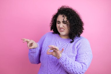 Genç, güzel bir kadın pembe arka plan üzerine sıradan bir süveter giyiyor. İğrenç bir ifade, tiksindirici ve tiksindirici bir yüz ifadesi. Çünkü tiksindirici bir tepki.