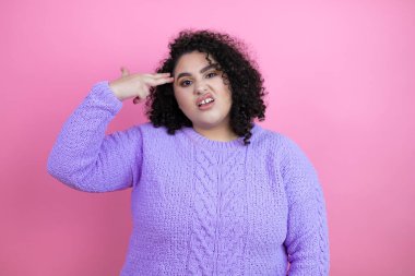 Genç ve güzel bir kadın pembe arka plan üzerine günlük süveter giyerek kendini vuruyor ve öldürüyor. Silah gibi el ve parmaklarını işaret ediyor, intihar jesti..