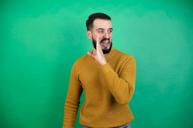 Yakışıklı bir adam yeşil arka plan üzerinden günlük giysiler giyer. Ağızdan ağıza el sürer. Gizli söylentiler yayar, kötü niyetli konuşmalar yapar.